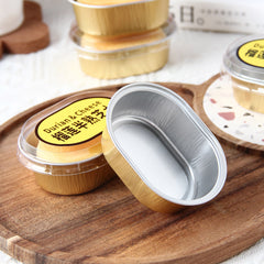 Foiltrust Oval aluminum mini cake or dessert containers with clear lids and yellow labels, shown on a wooden tray with other containers in the background.